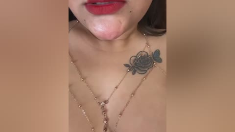 A close-up video of a woman with light skin, red lipstick, and a tattoo of a rose on her right shoulder, wearing a delicate gold necklace.