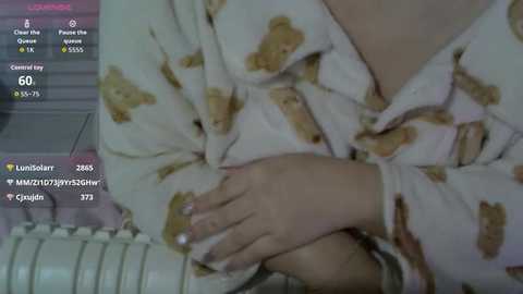 Video of a person in a white pajama shirt with a teddy bear pattern, wearing a ring on their left hand, sitting on a white radiator. Text on the left displays social media metrics.