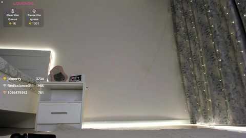 Video of a minimalist bedroom with white furniture, a small nightstand, and a bed with patterned curtains.