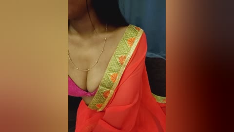 Video of a woman in a bright orange saree with a green border, revealing a pink bra. Her long black hair partially covers her face.