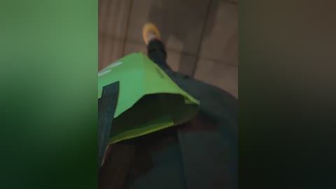 A blurry video of a person wearing a bright green umbrella in a dimly lit, possibly indoor setting. The background is indistinct, and the focus is on the vibrant umbrella.