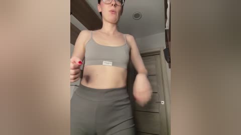 Video of a slender, fair-skinned woman with short hair, wearing a gray sports bra and leggings, punching the air in a dimly lit room.