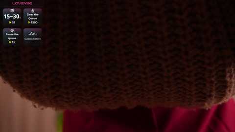 Video of a close-up, textured, dark brown sweater with a soft, knitted pattern. The sweater is worn, with visible wear and slight pilling. The background is blurred, showing a pink fabric, likely a shirt or blanket.