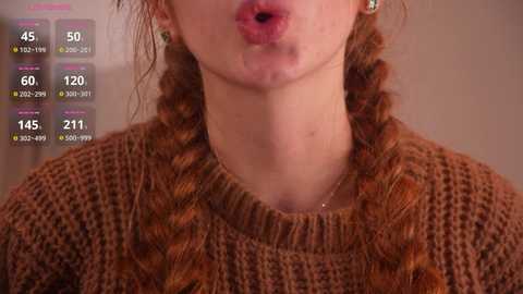 Video of a young woman with fair skin, wearing a textured brown sweater, kissing the air. Background features a blurred indoor setting and a digital health tracker overlay showing heart rate, steps, and calories.