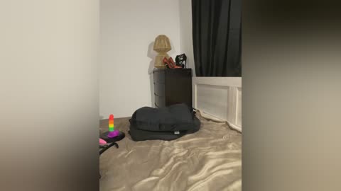 Video of a minimalist room with a beige rug, a black pillow, a small toy figurine, and a colorful, abstract, multi-colored sculpture near a dark curtain.