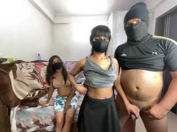 Video of three women in a bedroom: one wearing a face mask and black top, another in a floral bikini, and a third in a black mask and top, revealing her stomach.