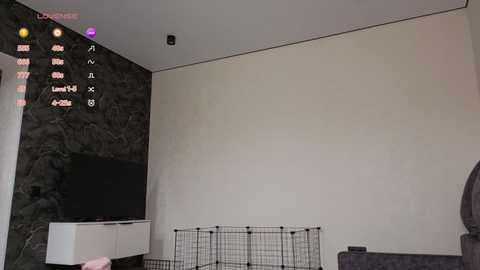 Video of a modern living room with a large flat-screen TV on a white stand against a dark marble wall, a black wire cage in the foreground, and a menu screen displaying video game options in the top left corner.