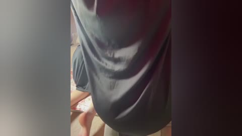 A video of a person wearing a dark gray t-shirt and light beige shorts, partially blurred, standing in a dimly lit room with a red wall.