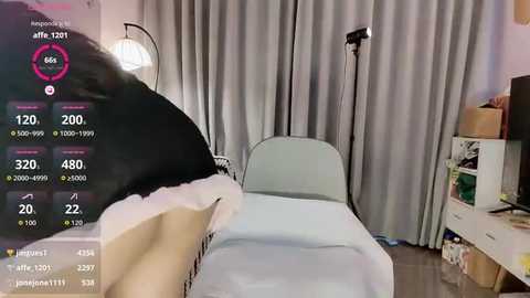 Video of a modern hospital room with a black-haired patient in a white hospital gown lying on a bed, surrounded by medical equipment and a desk with a computer monitor displaying a social media app.