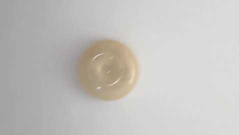 A close-up video of a single, beige, circular button or knob against a plain white background. The button has a glossy texture and a slight depression in the center. The image is simple and minimalistic, focusing solely on the object.