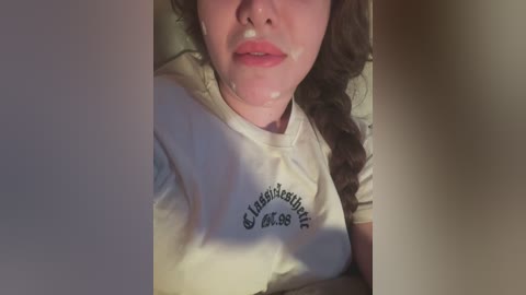 Media: Video of a woman with light skin, wearing a white t-shirt, lying down, with semen on her face, showing her partially exposed breasts.