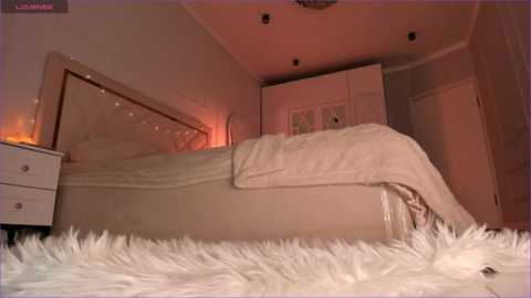Video of a cozy, feminine bedroom with beige walls, white fluffy rug, cream bedding, mirrored headboard, and string lights.