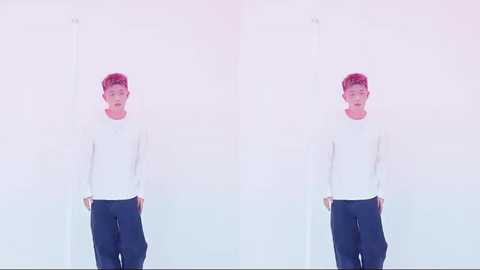 Video of a young man with pink hair, wearing a white sweater and navy pants, standing in front of a white, minimalist background.