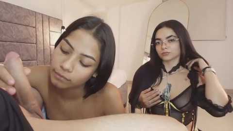 Video of a young Latina woman with long black hair, topless, performing oral sex on a man's erect penis in a bedroom.