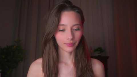 Video of a young Caucasian woman with long brown hair, fair skin, and closed eyes, standing in a dimly lit room with a blurred background.