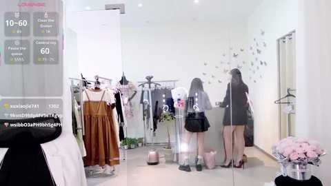 Media: Video of a modern clothing store with white walls, clear display cases, and mannequins wearing transparent raincoats. Pink flowers decorate the floor, and shoppers browse the merchandise.